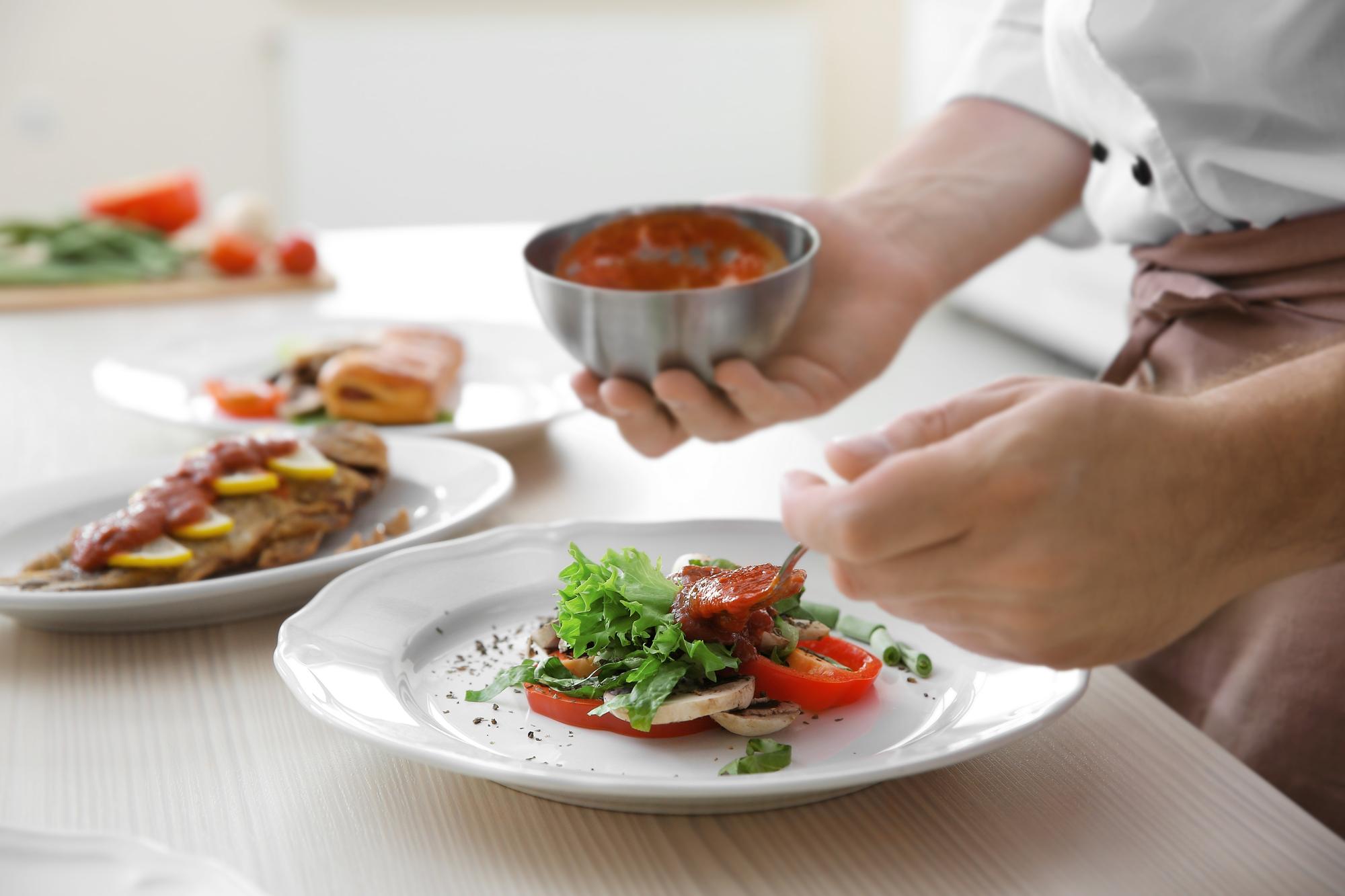 Seated chef preparing a plated dish in warm kitchen